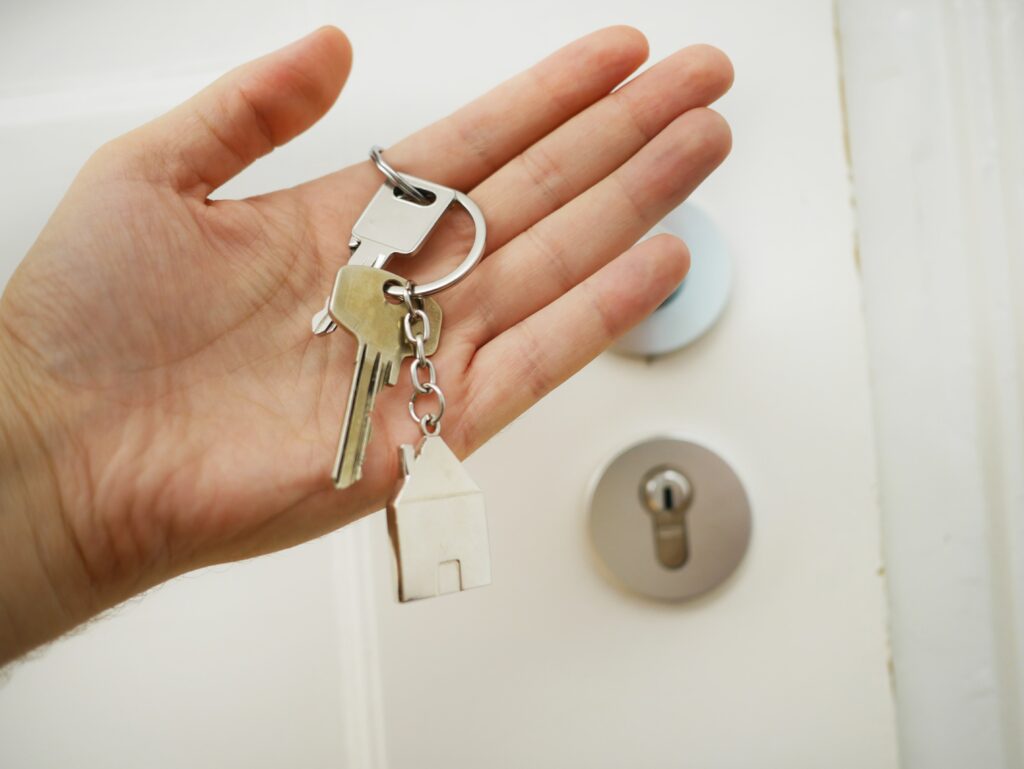 Person Holding Keys with House Keyring In Front Of Door